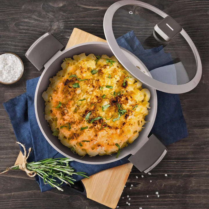 Brown casserole dish with glass lid open to show macaroni and cheese, with salt and rosemary herbs