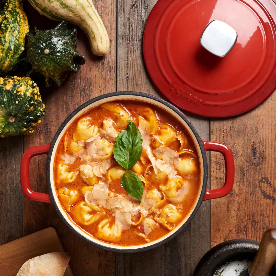 Overhead view of a heavy red casserole dish filled with a pasta bake meal, on a dark wooden table