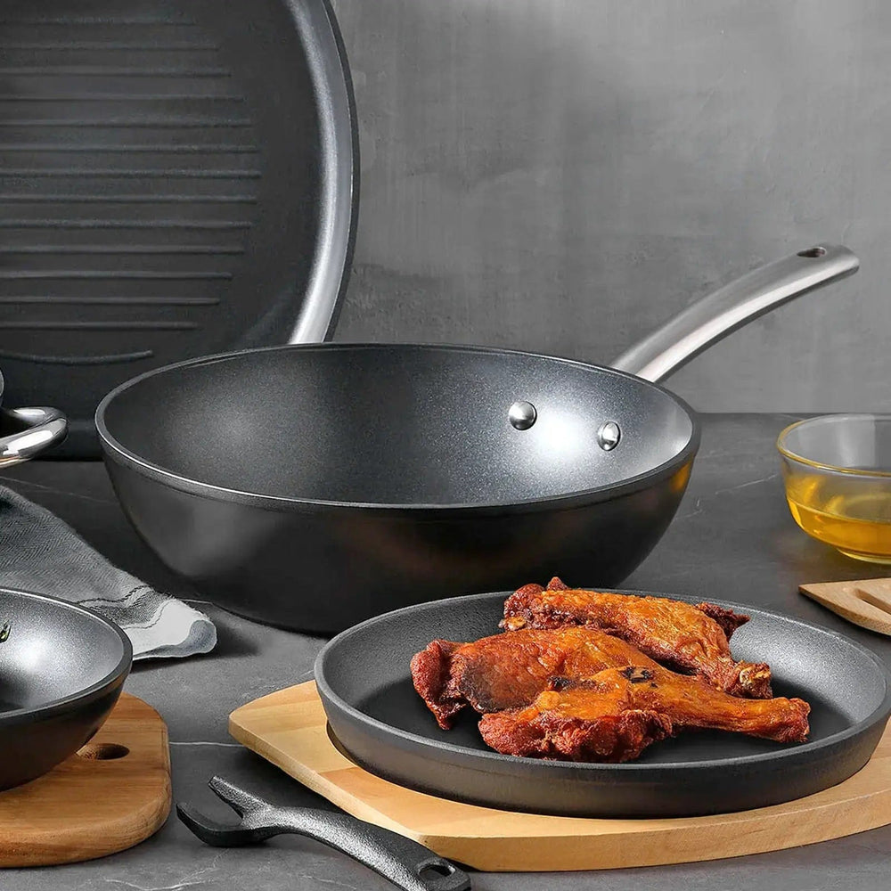 Black non-stick wok on a table with pork chops on a plate