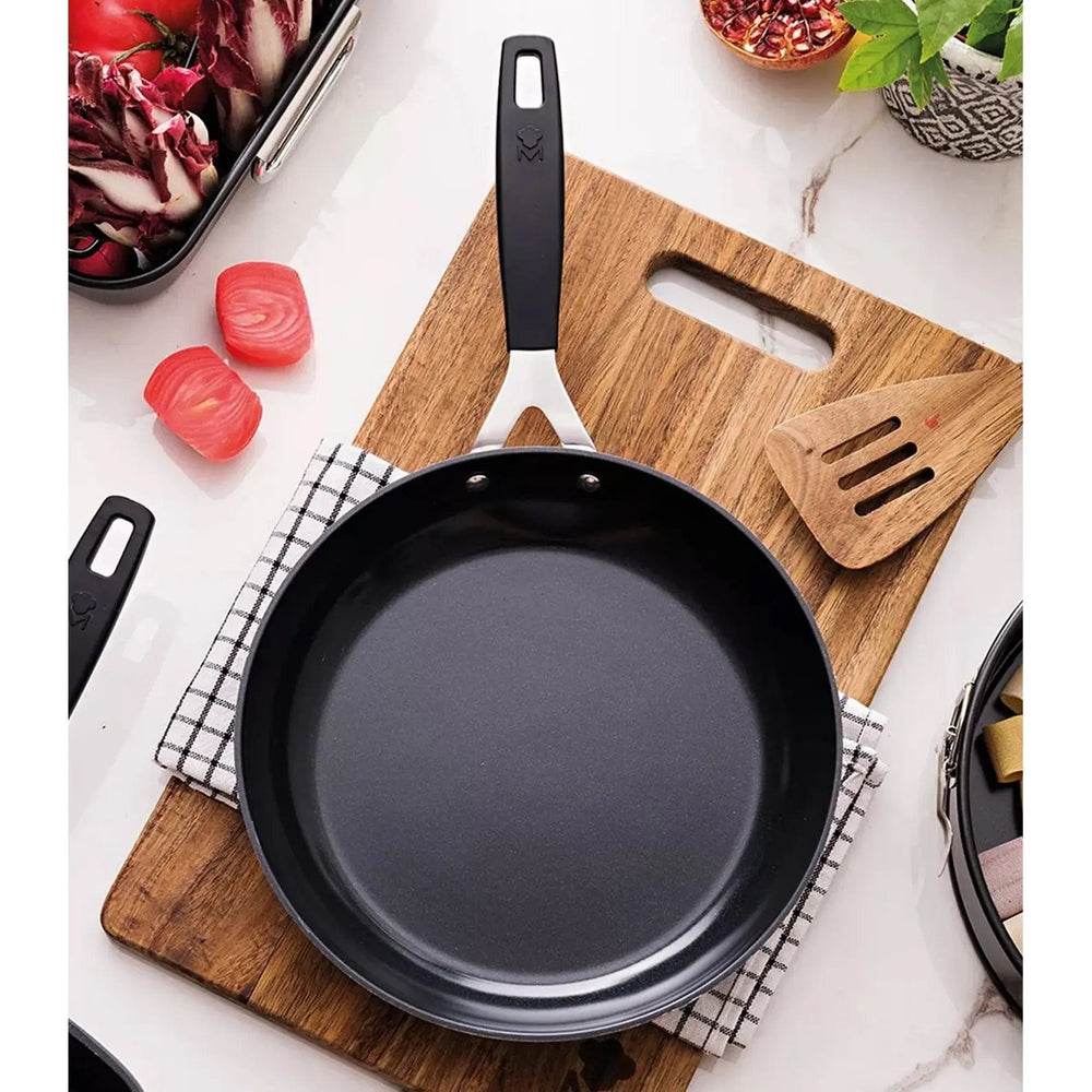 Frying pan sitting on a wooden chopping board and dish towel, beside food dishes