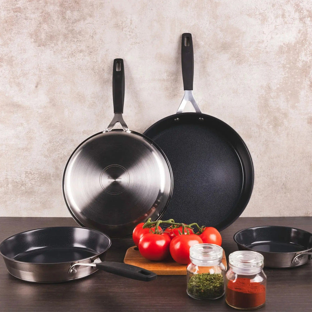 A range of frying pan sizes on a kitchen worktop with tomatoes ands spice jars