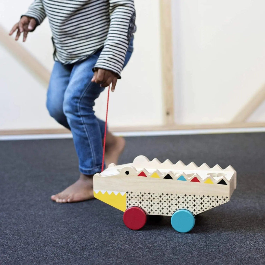 Young child pulling along a brightly coloured wooden alligator toy