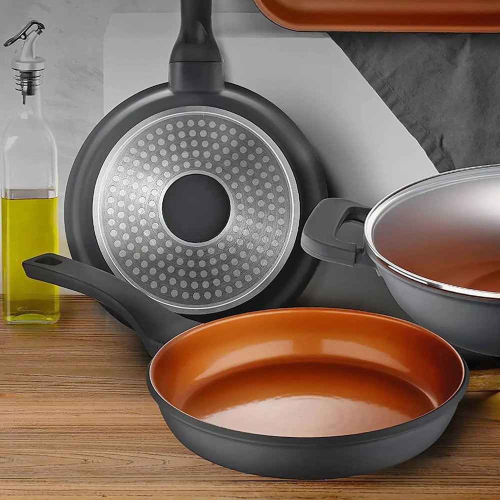 Bronze coated frying pan on a wooden worktop with casserole dish and pan showing dot induction base