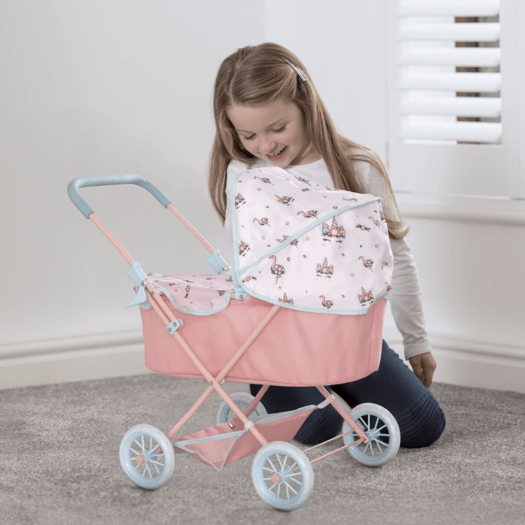 A Young girl kneeling playing with her pink toy pram with light blue handles, showcasing a white canopy adorned with flamingo, flower, and butterfly designs.