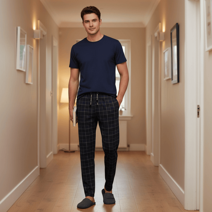 Man wearing a navy t-shirt and plaid pants standing in a hallway.