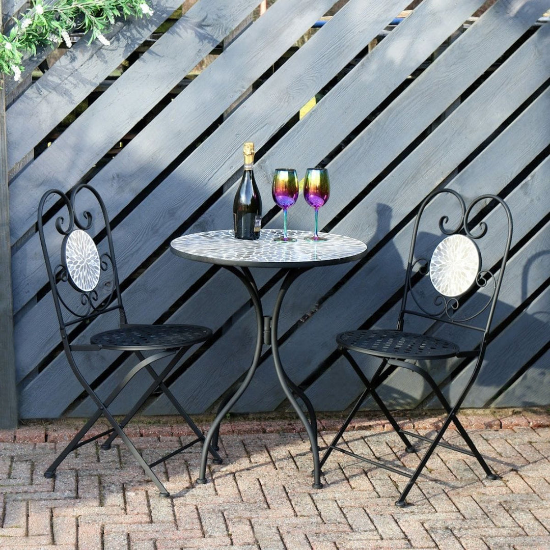 bistro set on brick patio space with blue coloured fencing in the background with iridescent glasses resting on top and foliage garland draped over fence