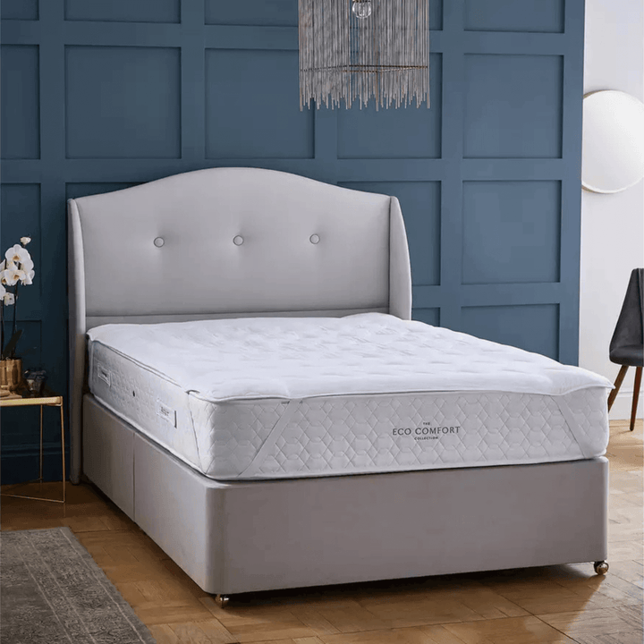 Gray bed with a mattress in a room with blue walls and wooden flooring.