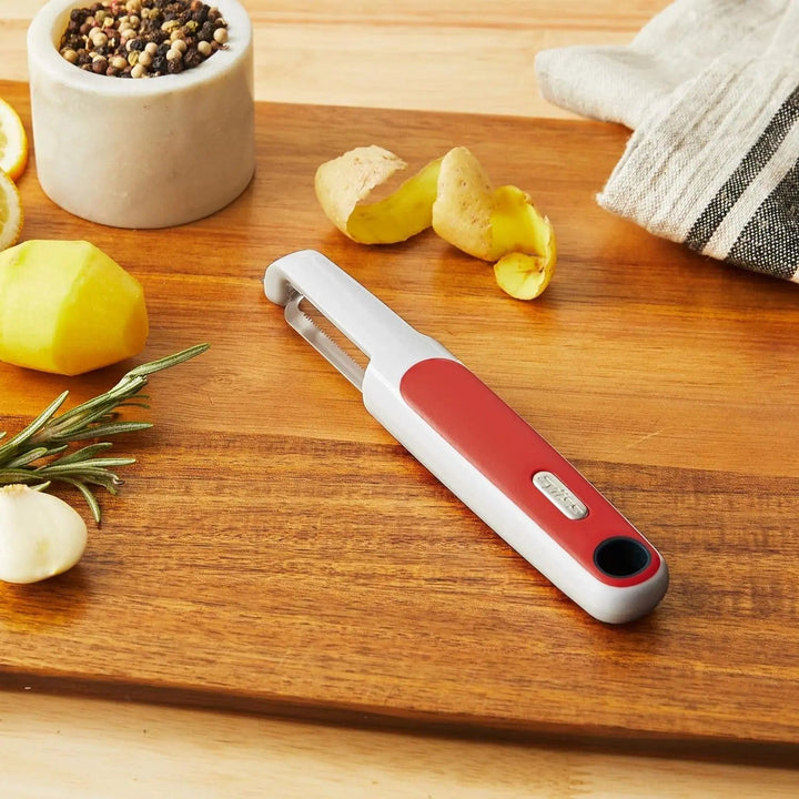 red and white kitchen peeler on a wooden board with potatoes and spices