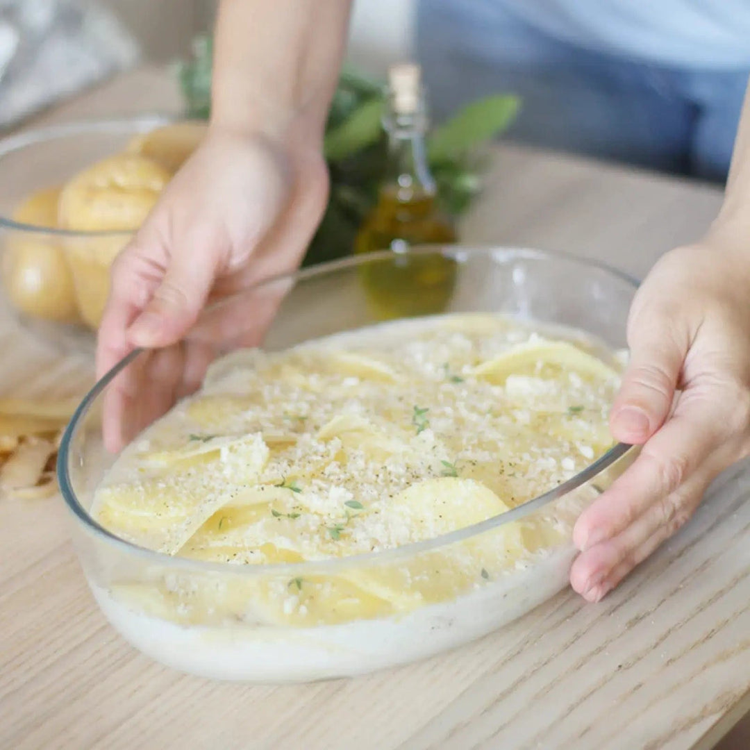 Hands holding a glass oval pie dish with food on a wooden table