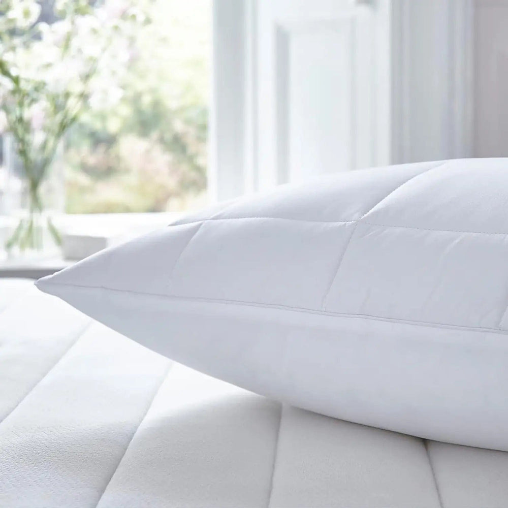 Quilted covered white pillow on a bed with vase of flowers and window