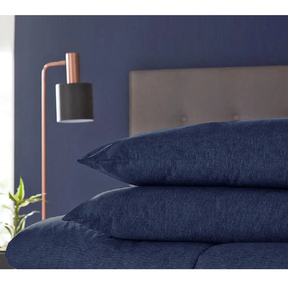 2 navy blue coverless style pillows on a bed, with bedside lamp