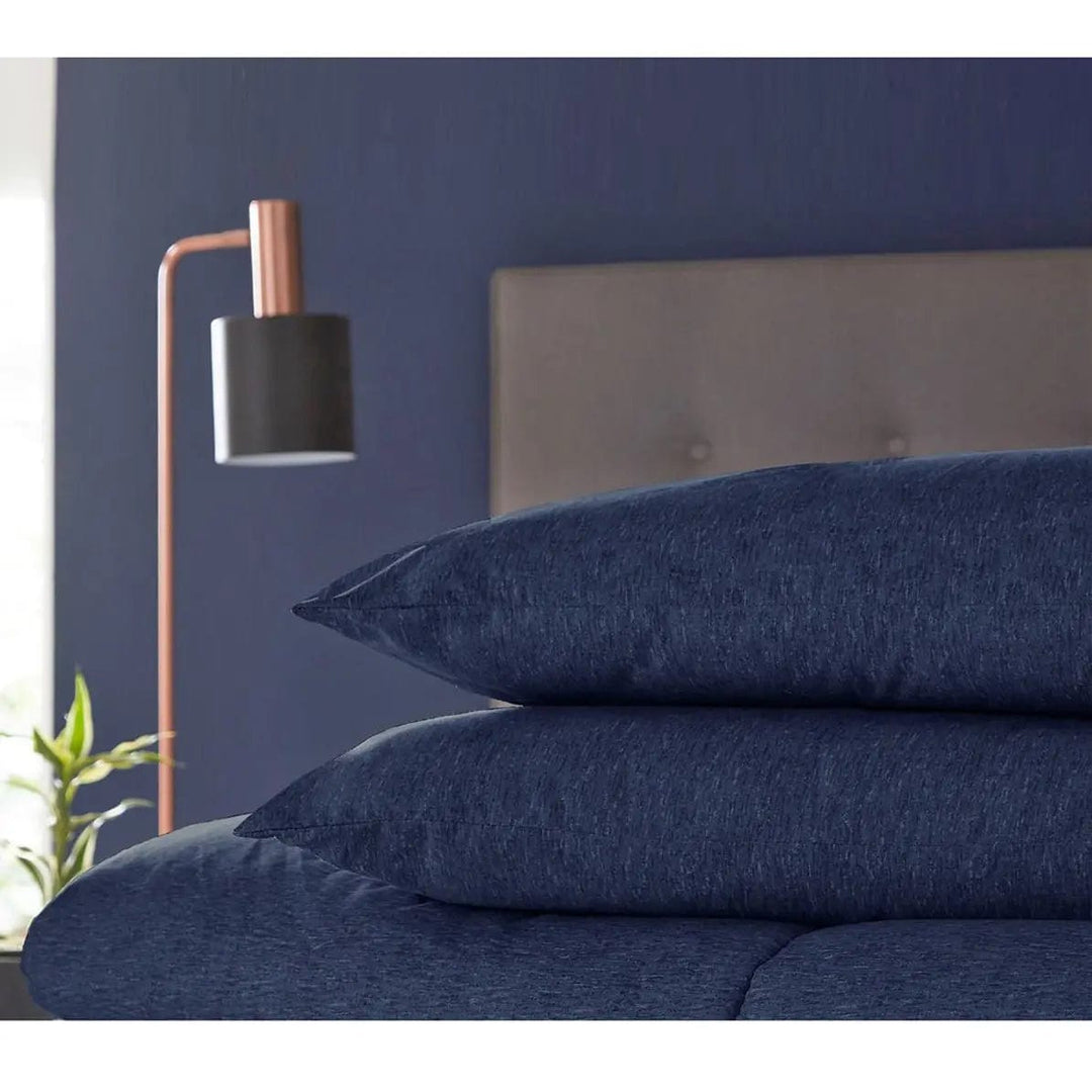 2 navy blue coverless style pillows on a bed, with bedside lamp