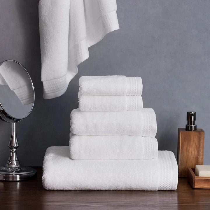 Set of 6 white towels on a dark table with shaving mirror and grey wall