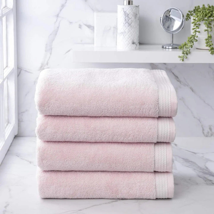 Set of 4 blush pink towels on a grey marble bathroom shelf with mirror and plant