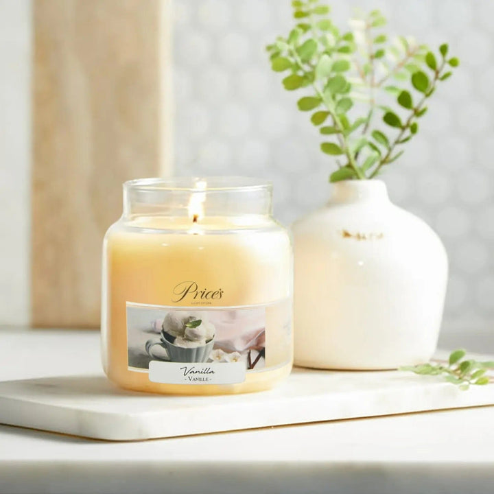 Price's Vanilla scented candle lit on a board with vase of foliage