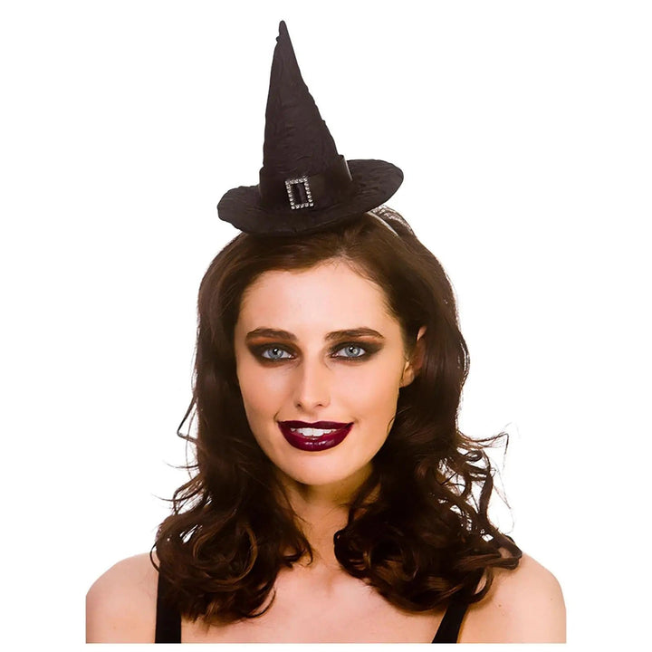 Woman wearing a mini witch hat on headbnd in black with silver diamante buckle detail for fancy dress costumes