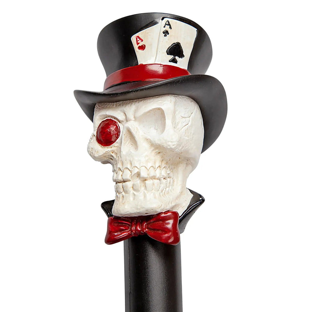 Close up of a white skull with red eye, red bow tie and a black top hat with 2 aces playing cards