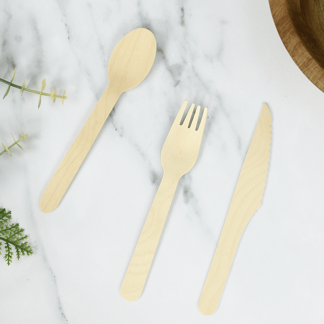 wooden spoon, wooden fork and wooden knife on marble worktop besude dark brown wooden bowl and artificial foliage