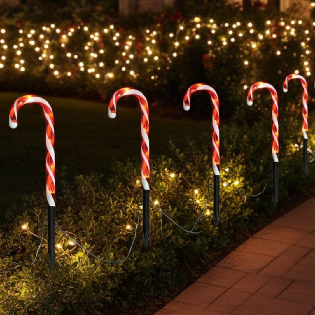 Decorative candy cane lights on stakes with a garden and string lights in the background.