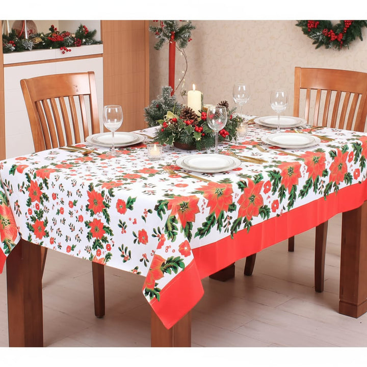 Christmas poinsettia tablecloth on a wooden table set for Christmas dinner with glasses and candles
