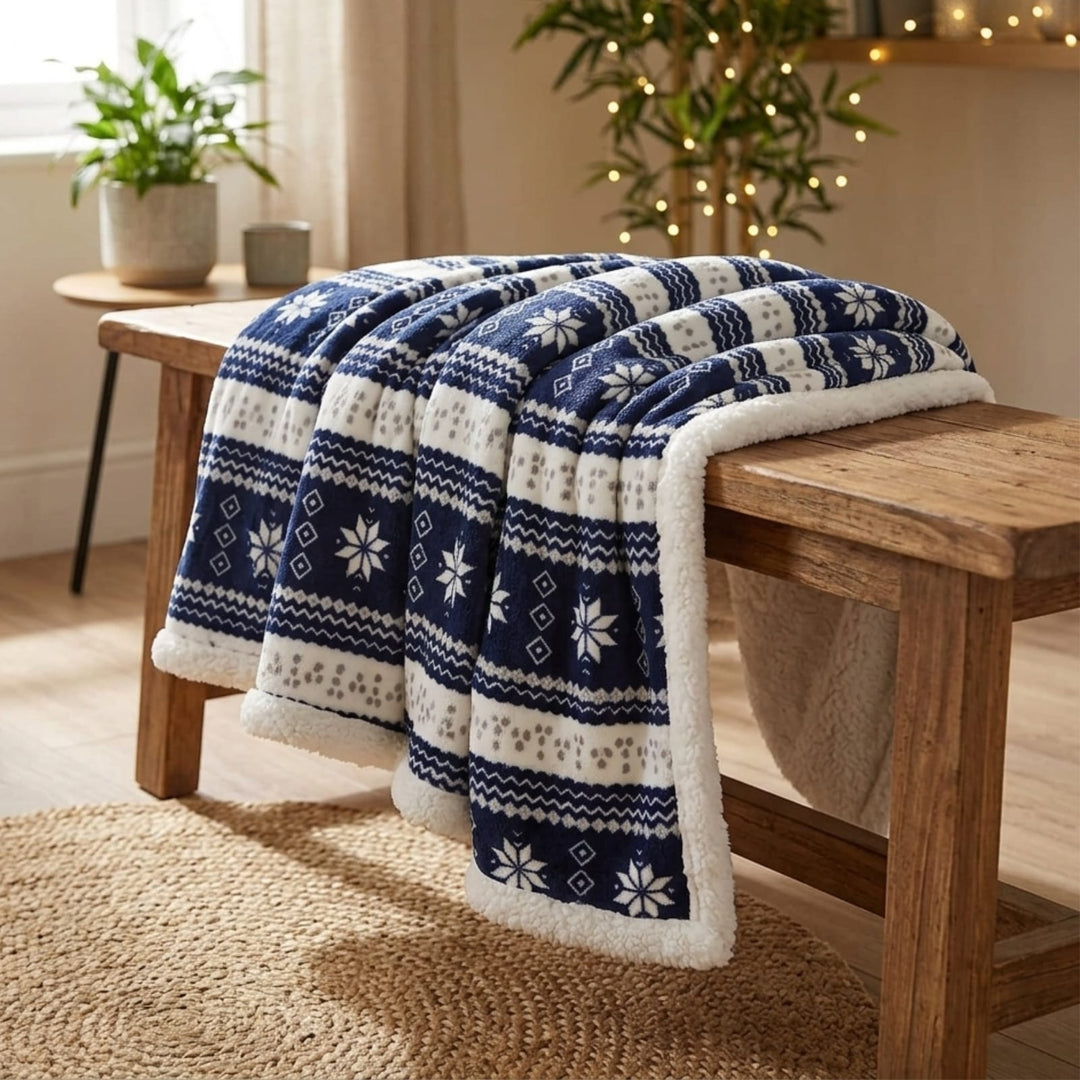 A cozy navy and cream Nordic-patterned throw blanket with a plush sherpa lining is draped over a rustic wooden bench in a warmly lit living room.