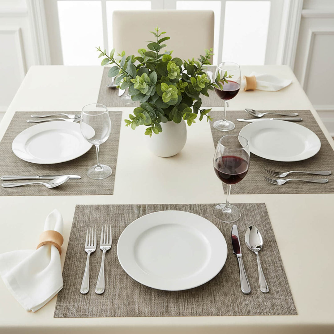 Dining table set with 4 coffee colour place mats, white plates cutlery and foliage centre piece