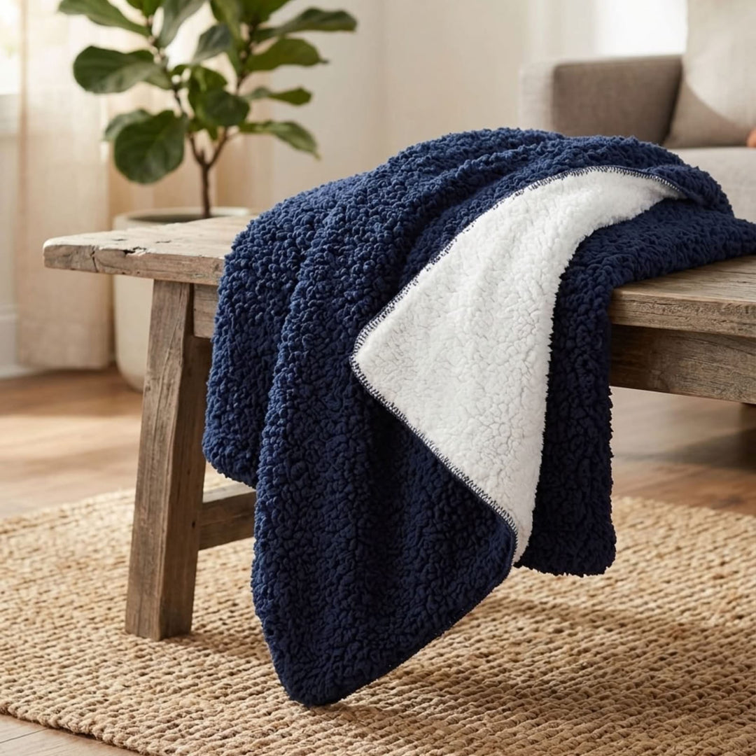 A navy blue sherpa throw blanket with a white sherpa reverse side draped over a rustic wooden bench in a cozy living room setting.