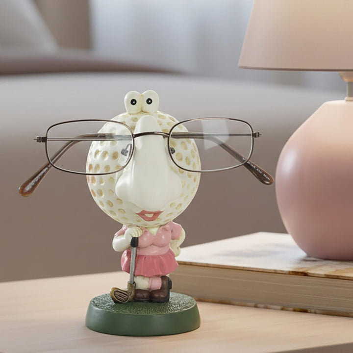 Novelty lady golfer figure reading glasses holder sitting on a bedside table with pink lamp