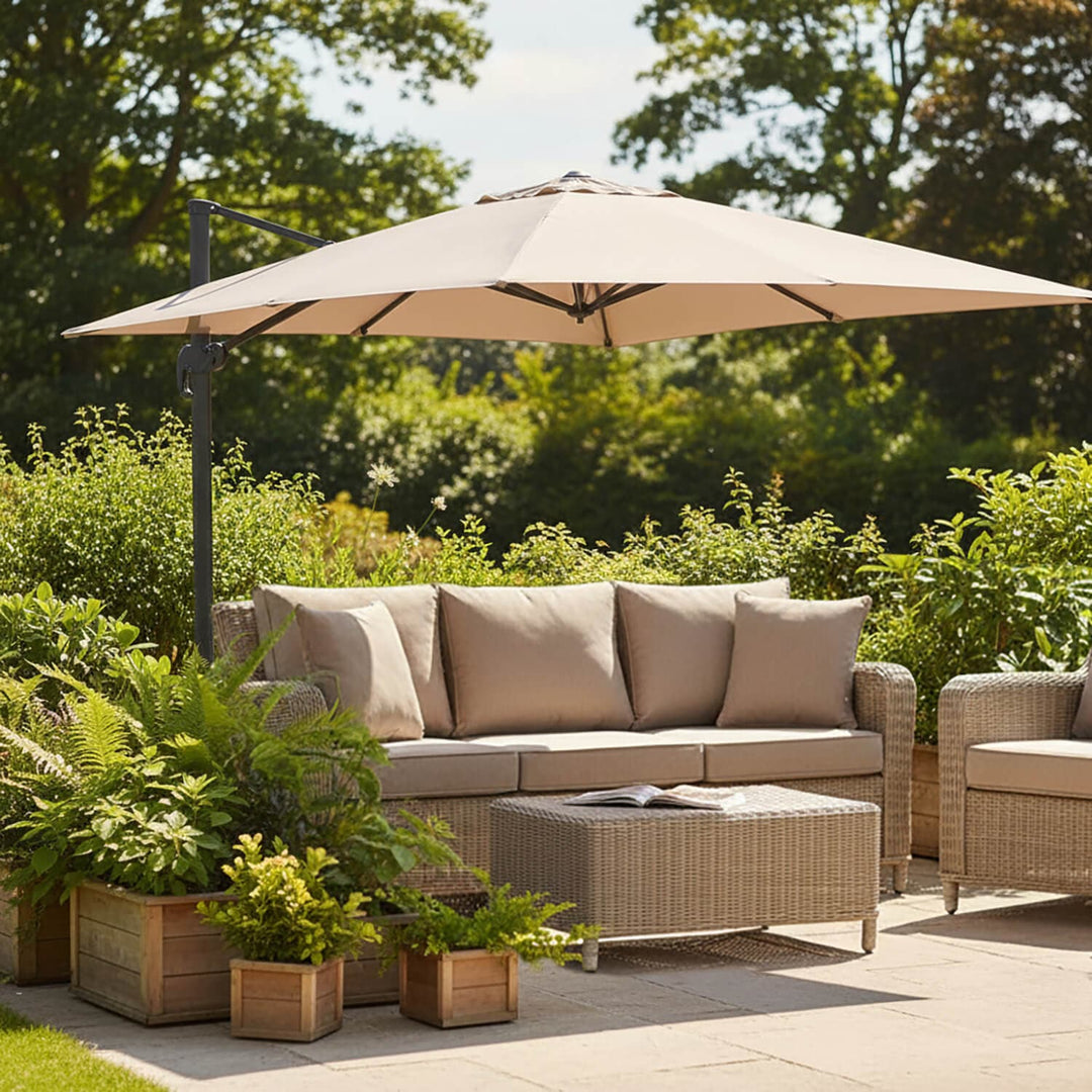 Outdoor patio setting with a large beige parasol, sofa, and ottoman surrounded by plants.