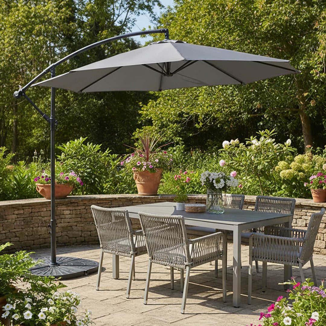 Outdoor patio set with a large grey banana style parasol, table, and chairs in a garden setting.