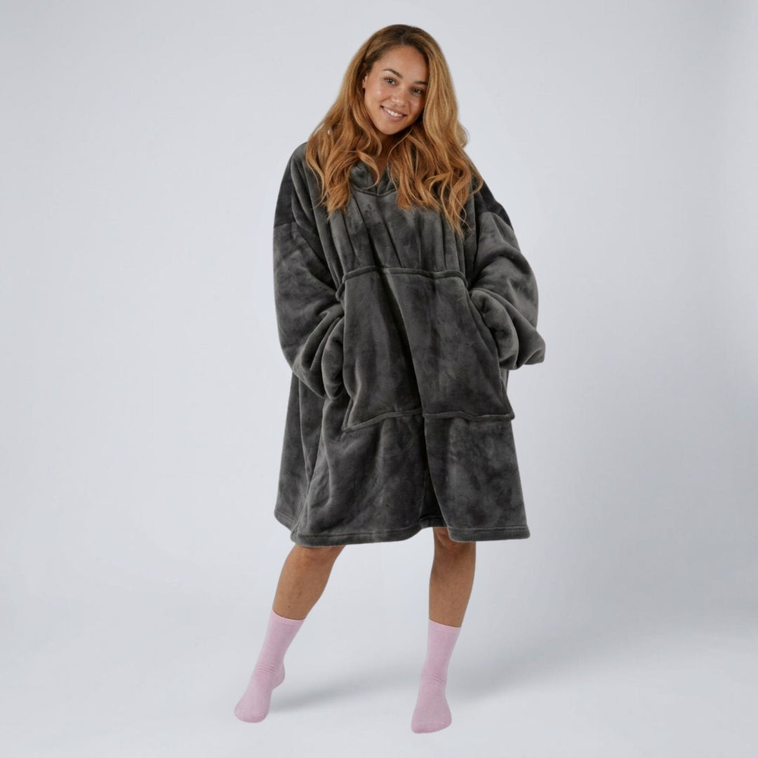 A woman modeling a plush, oversized dark gray fleece robe with pockets, paired with light pink socks, against a light gray studio background.