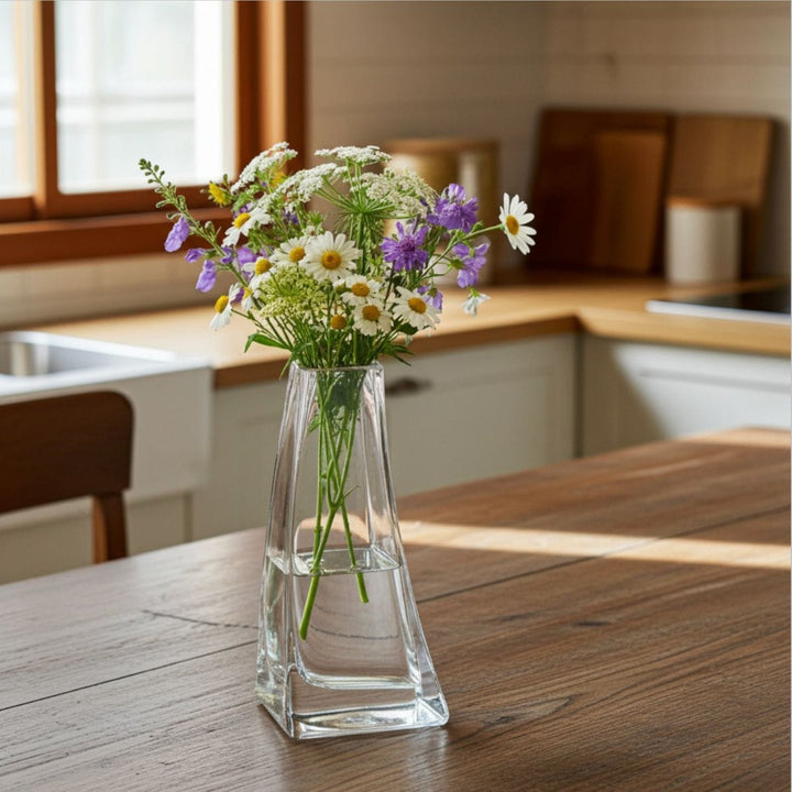 Clear glass vase with flowers on a wooden table in a kitchen