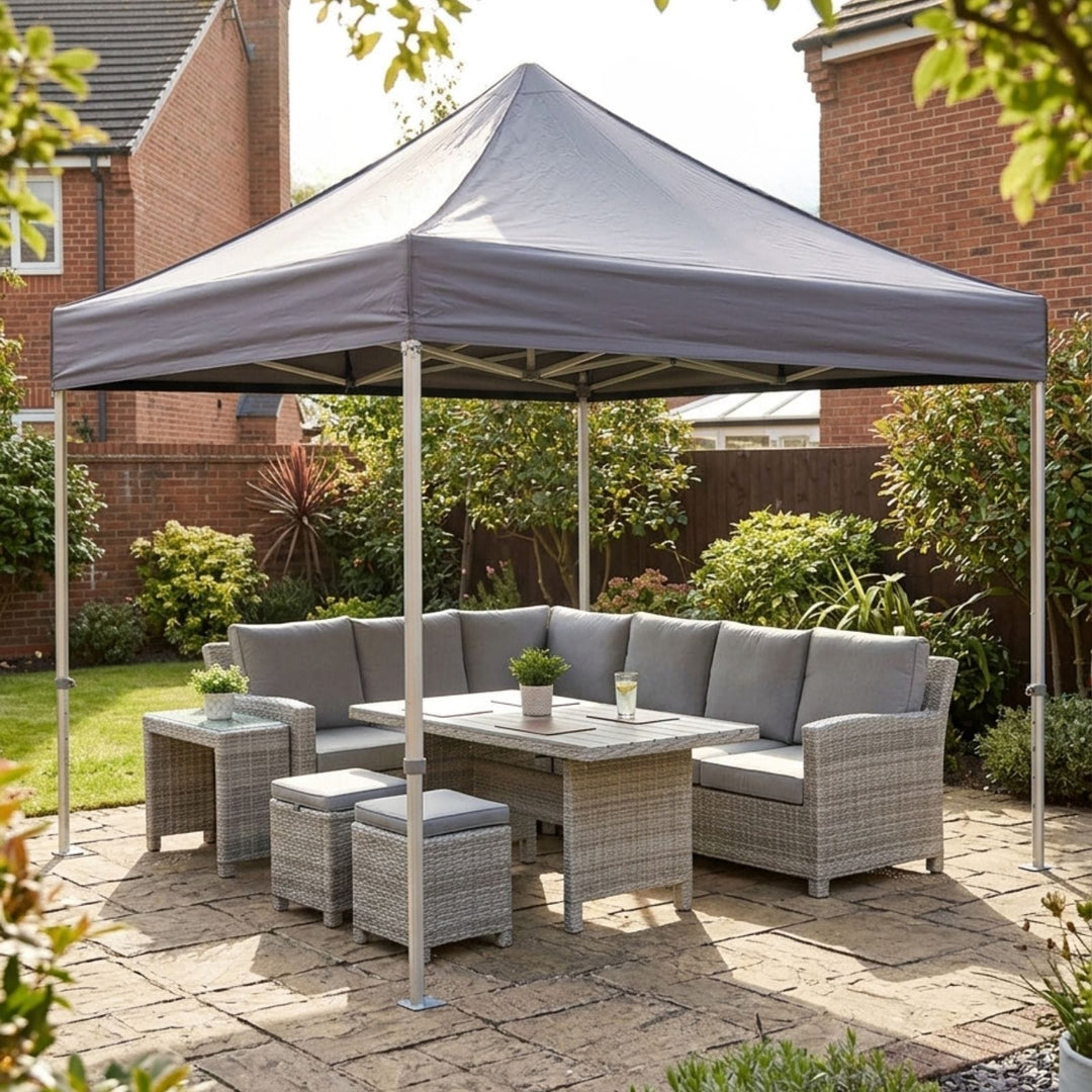 Gray outdoor patio gazebo canopy with a matching wicker patio sofa, table, and two ottomans, set on a stone patio in a backyard garden.
