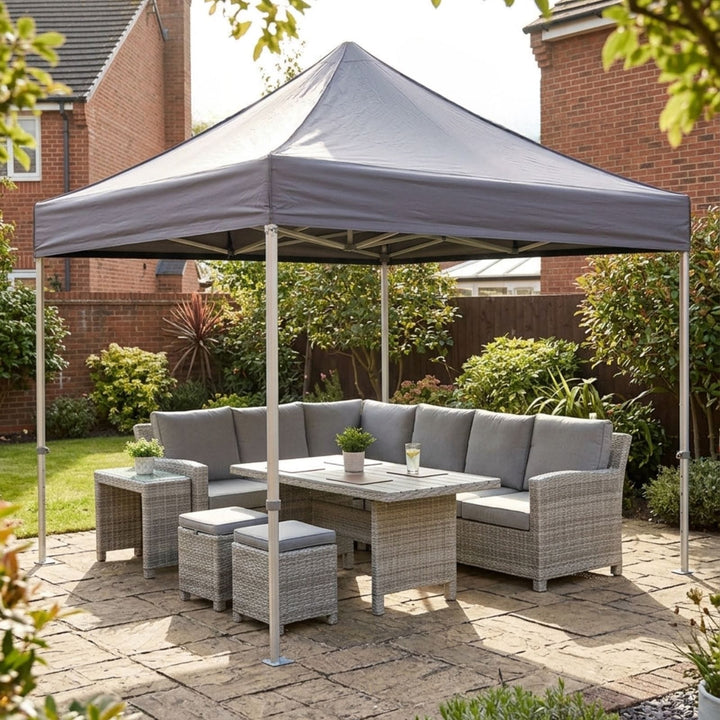 Gray outdoor patio gazebo canopy with a matching wicker patio sofa, table, and two ottomans, set on a stone patio in a backyard garden.