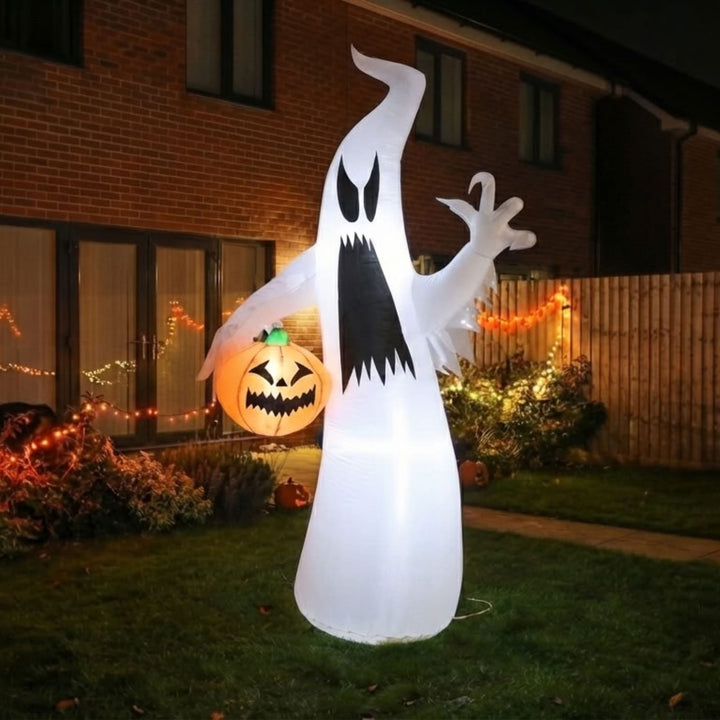 A large inflatable ghost Halloween decoration stands on a lawn in front of a house at night, glowing with warm light. The ghost is white with a black mouth and eyes, and a jack-o&