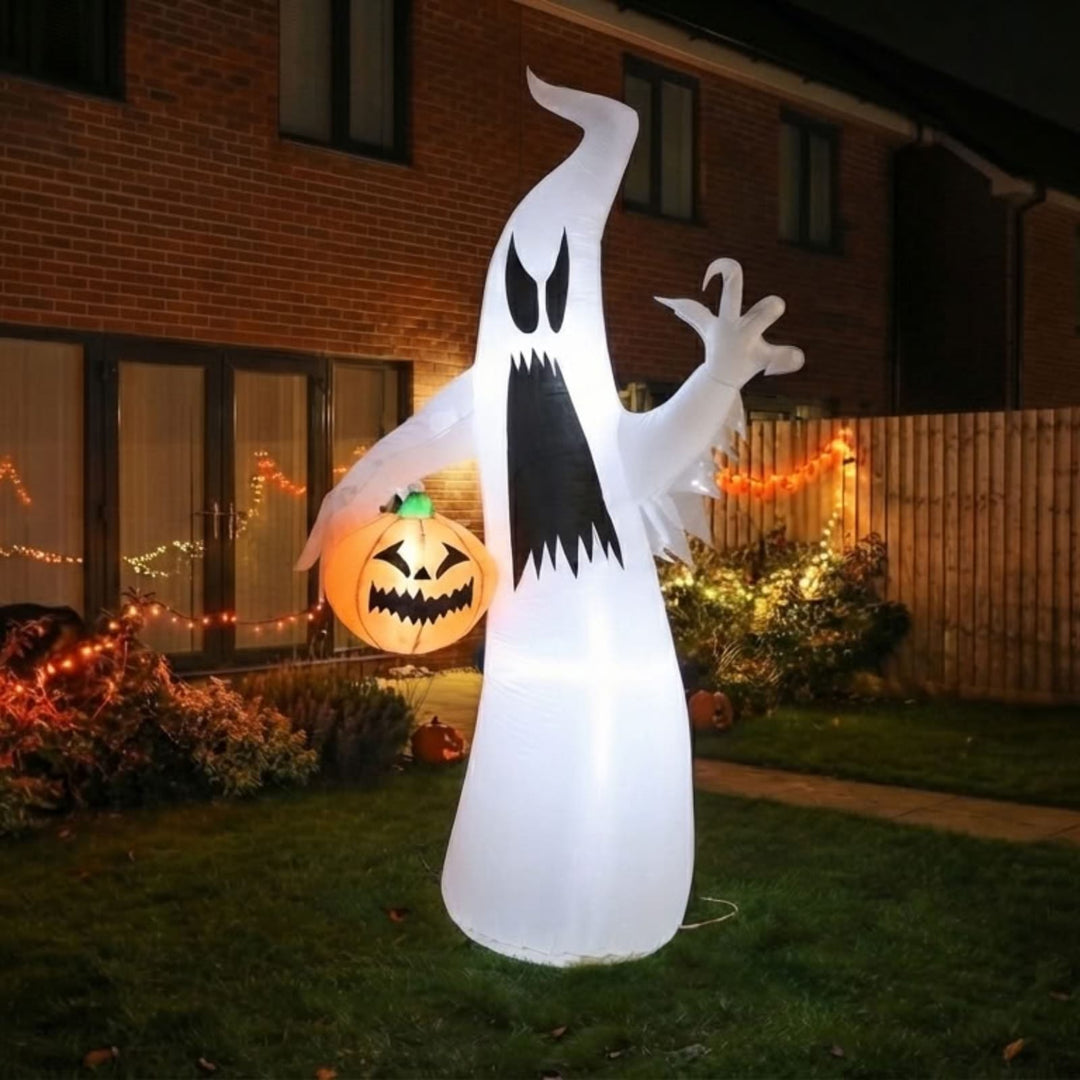 A large inflatable ghost Halloween decoration stands on a lawn in front of a house at night, glowing with warm light. The ghost is white with a black mouth and eyes, and a jack-o&