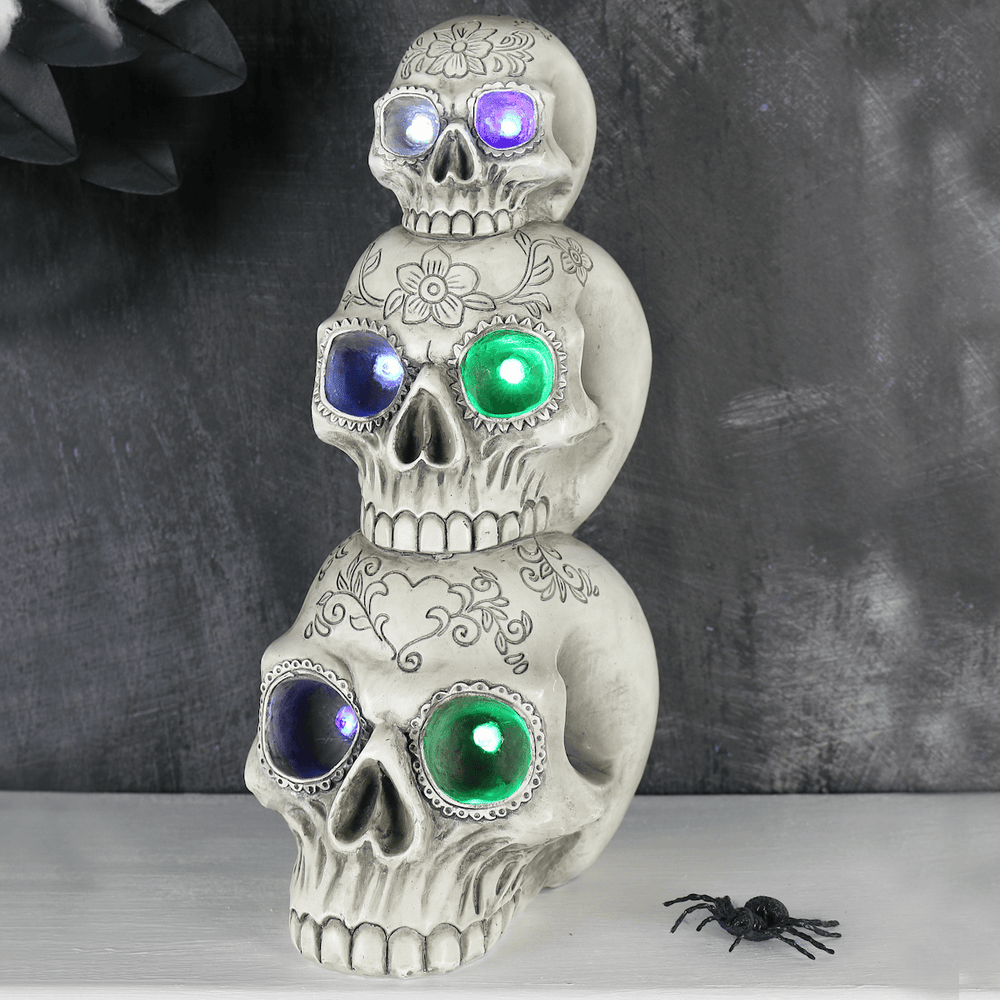 A stacked three-skeleton Halloween decoration with glowing LED eyes in purple, blue, and green, displayed on a white surface against a dark gray background.