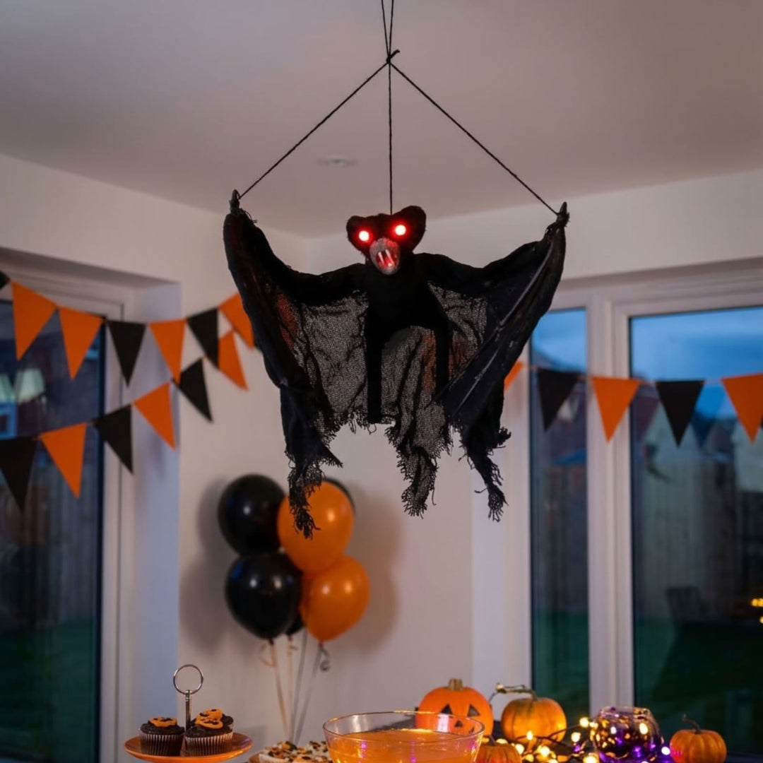bat decoration hanging from ceiling in room with snack table underneath and halloween bunting in background