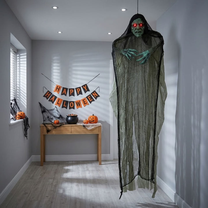 A large hanging Halloween decoration shaped like a ghostly figure draped in tattered black gauze, with a green face and glowing red eyes, displayed in a staged hallway with a &
