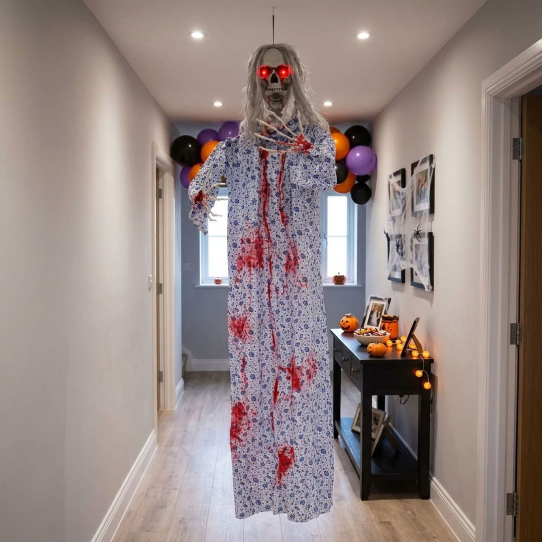 A Halloween hanging decoration of a creepy ghostly figure with a skull mask, red glowing eyes, and a long floral nightgown splattered with red blood, displayed in a residential hallway decorated for Halloween.