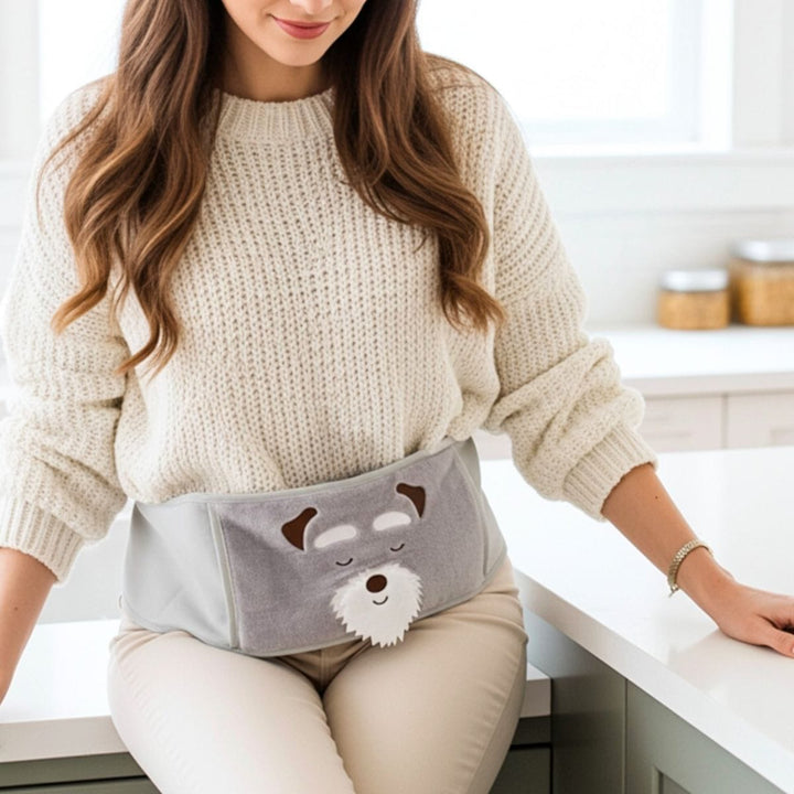 Woman wearing a gray heating pad with a dog cartoon design on a kitchen counter.