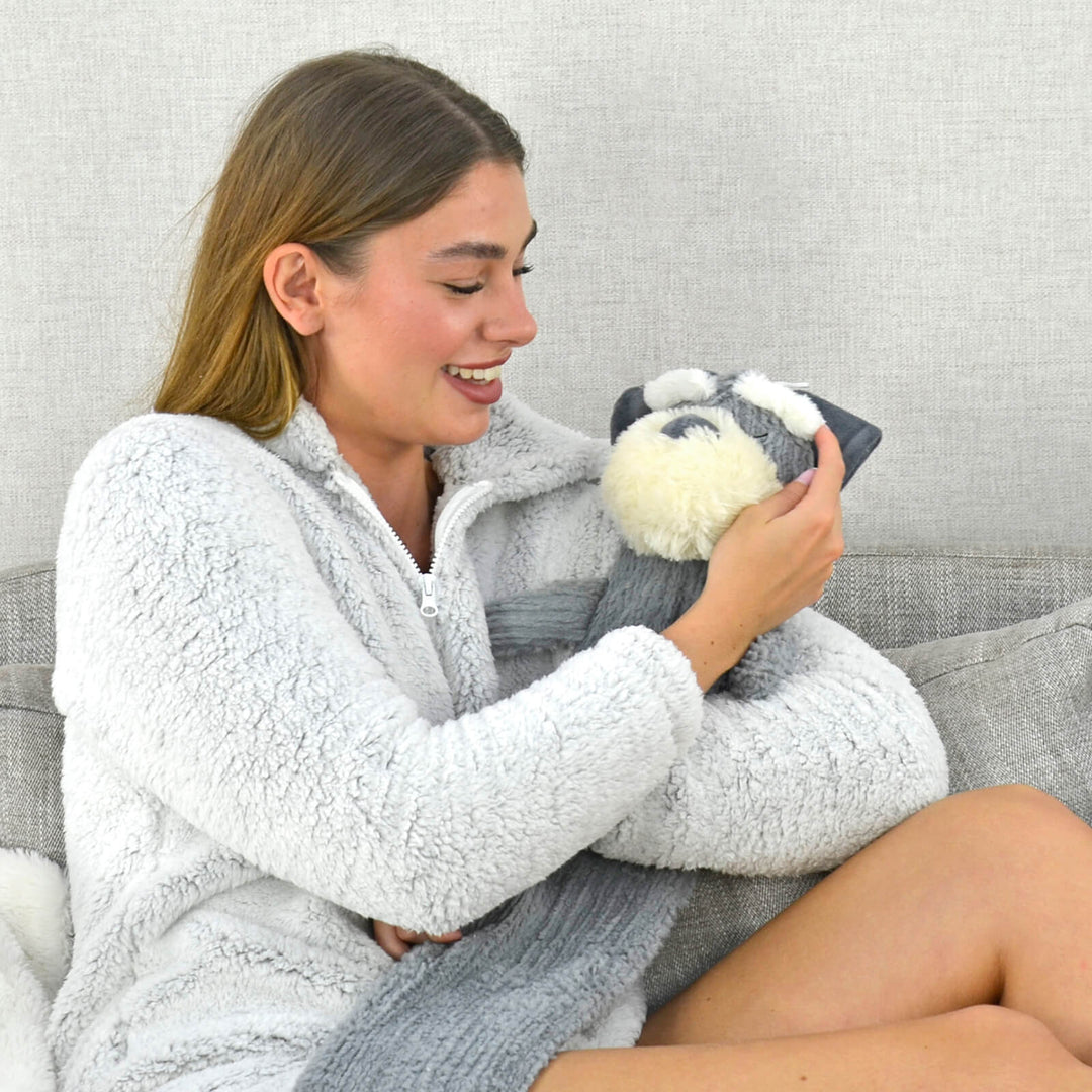 Woman sitting on a sofa cuddling a long hot water bottle with grey dog fleece cover