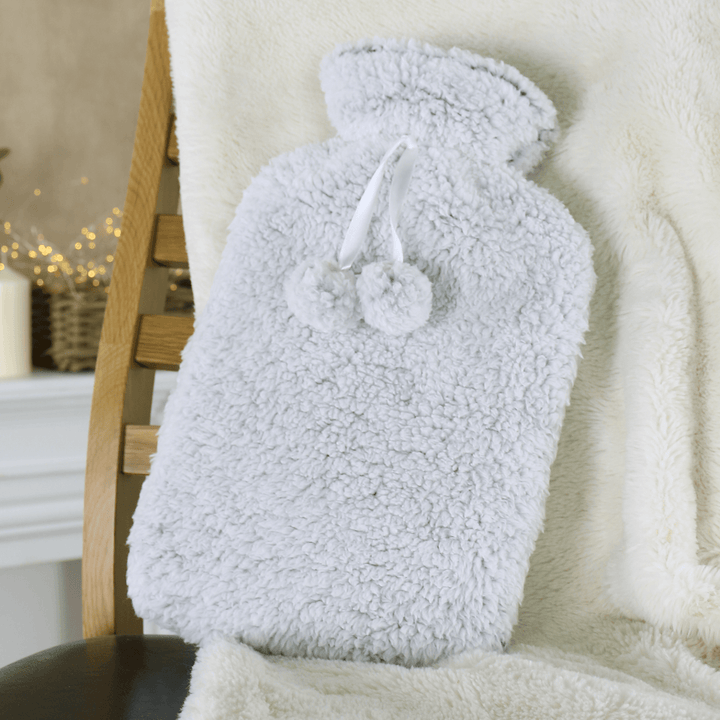 grey fleecy hot water bottle resting on chair with fairy lights in the background