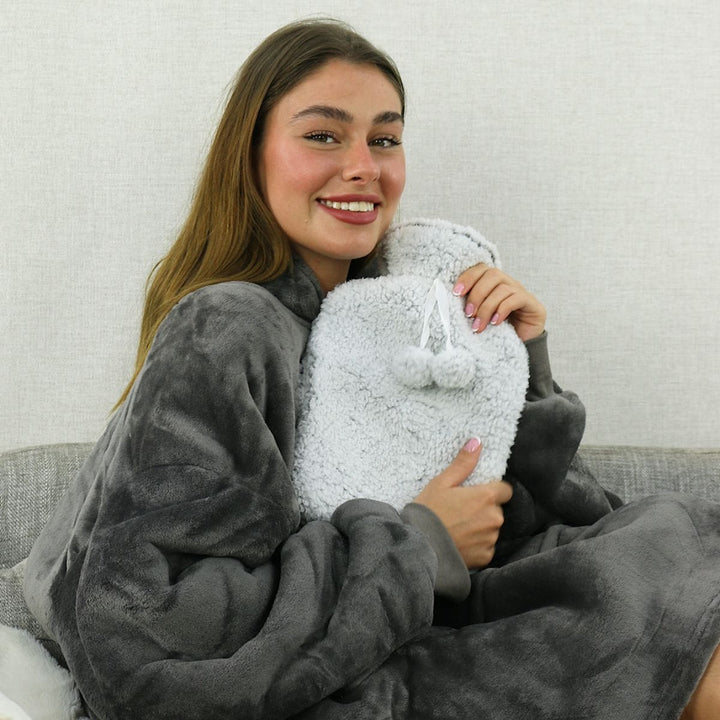 Woman in a dark grey dressing gown holding a grey fleece hot water bottle with pom poms