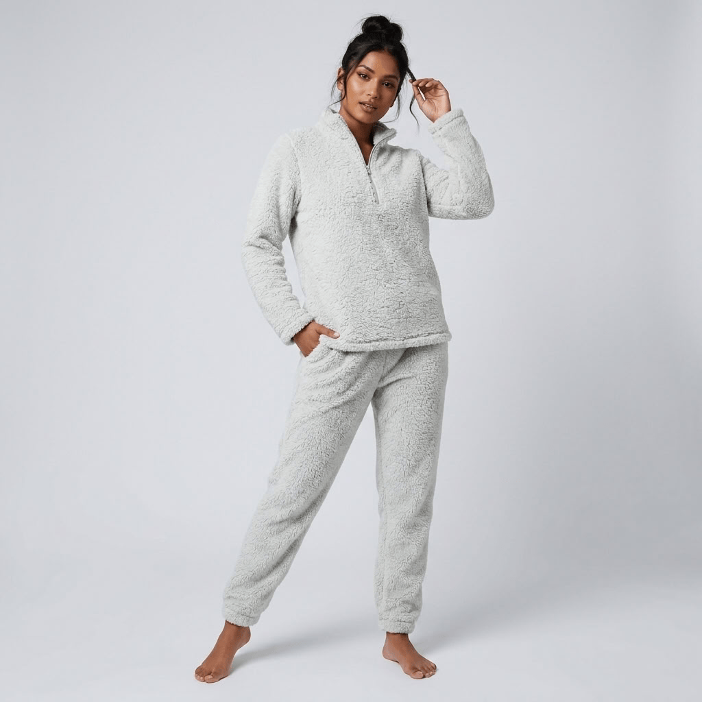 A woman modeling a light gray sherpa fleece pajama set consisting of a half-zip long-sleeve top and matching jogger pants, photographed against a neutral light gray studio background.