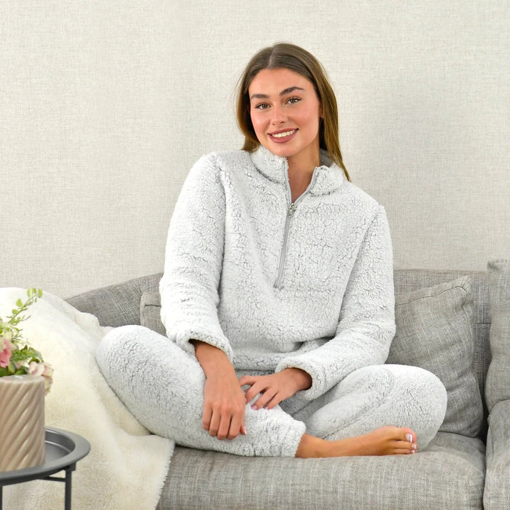 Young lady wearing light grey fleece PJs sitting cross legged on a sofa