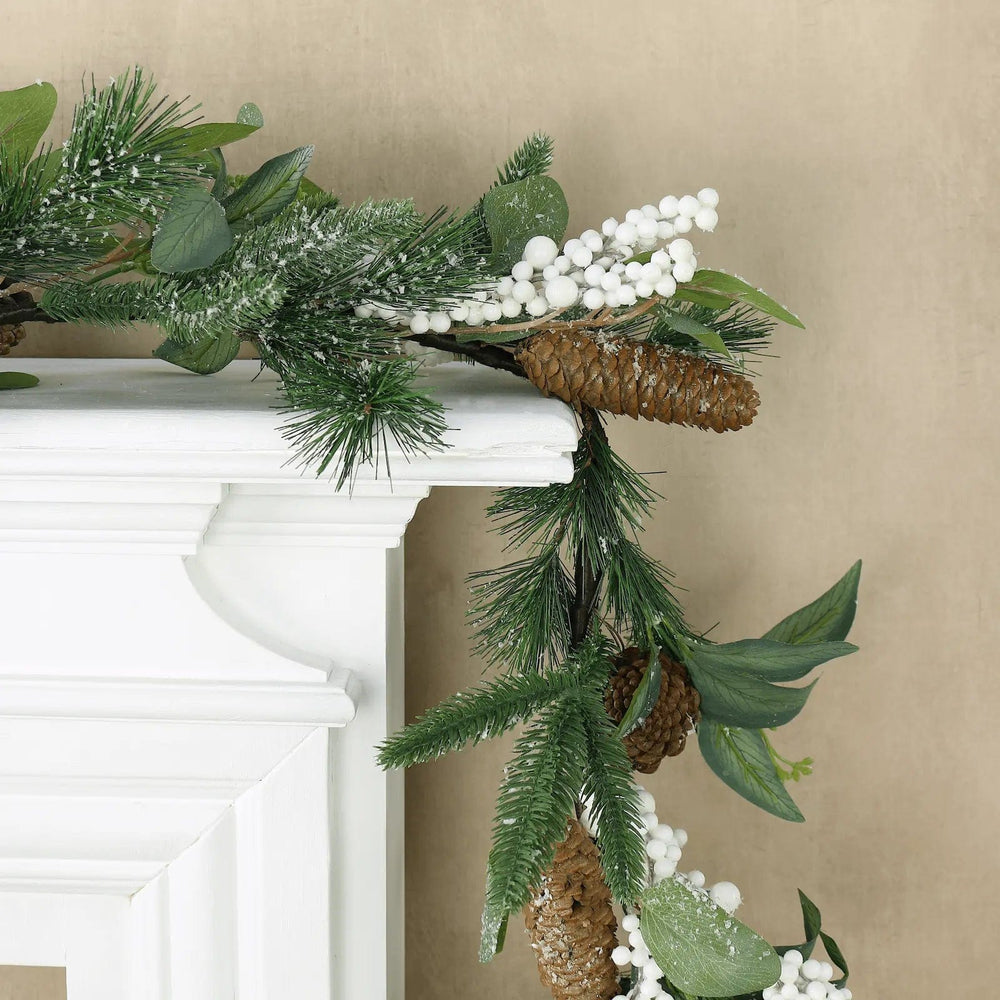 Christmas garland with white berries and pine cones draped over a white wood manteliece