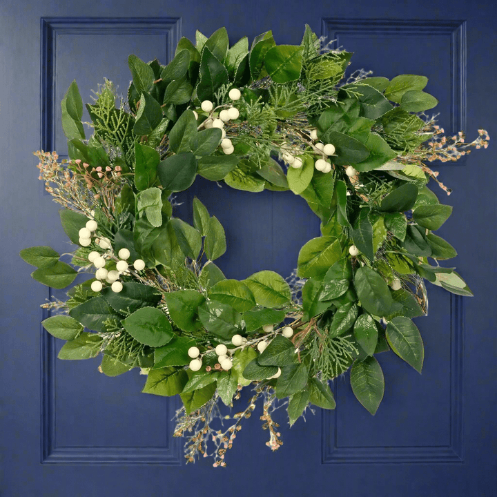 Green foliage Christmas wreath with white berries and little pink flowers on a Blue Door