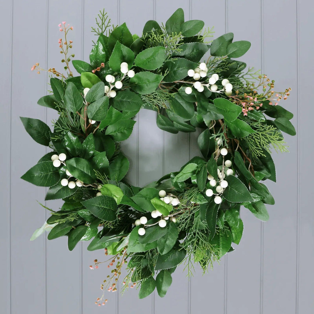 Artificial Christmas wreath with green leaves, white berries and pink flowers on a grey panelled wall