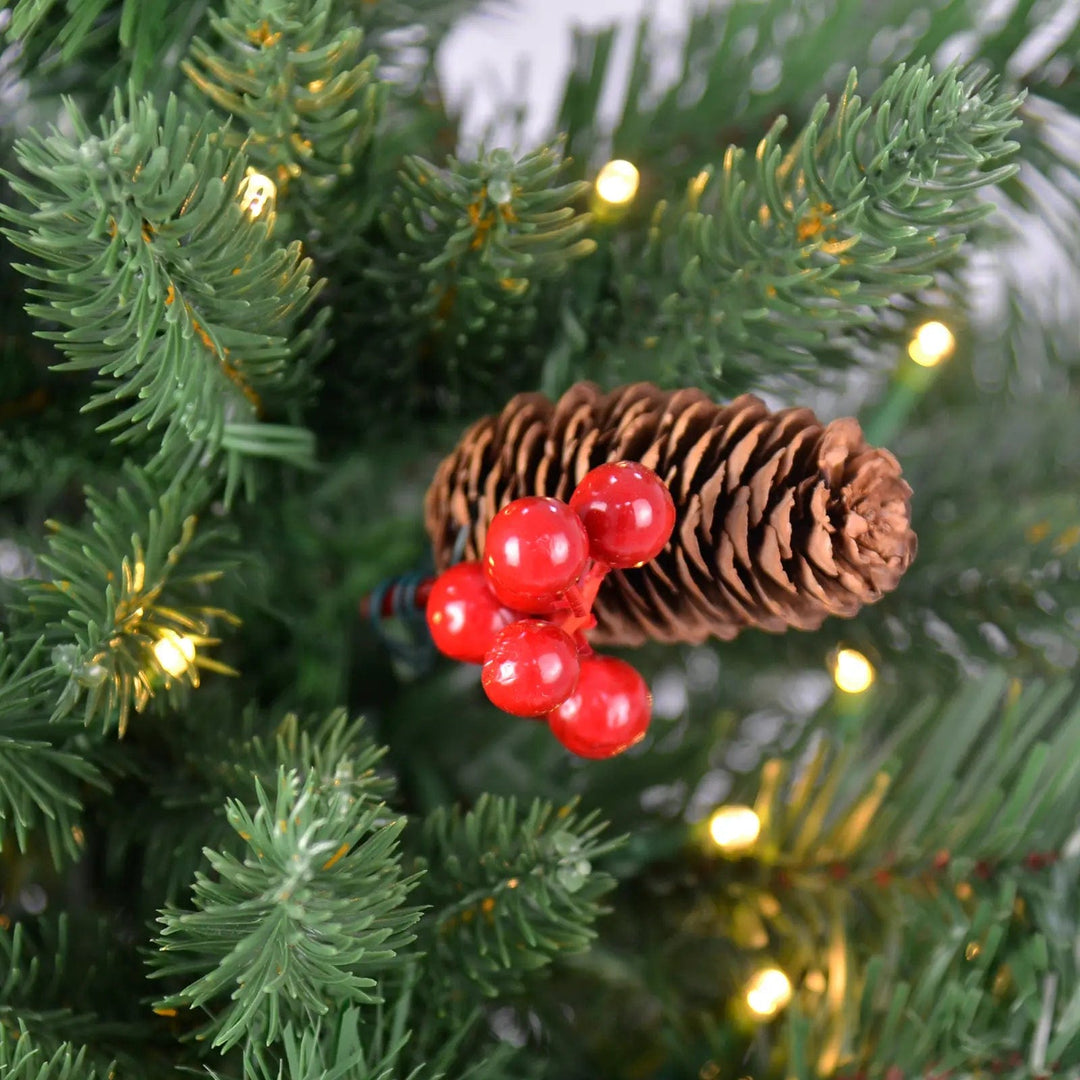 Close up of red berries and pine cone on a green pine Christmas tree with warm white fairy lights